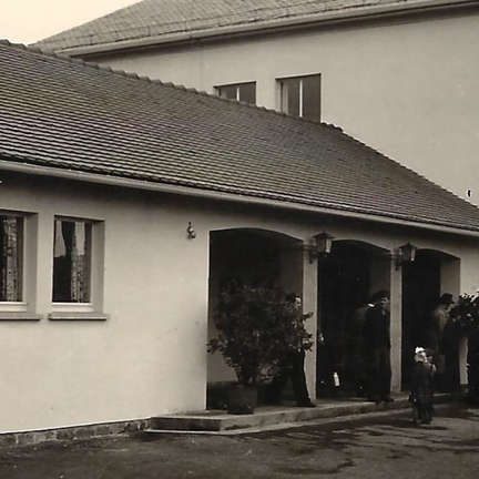 Ein schlichtes altes Gebäude mit Eingangsbereich und Personen davor.