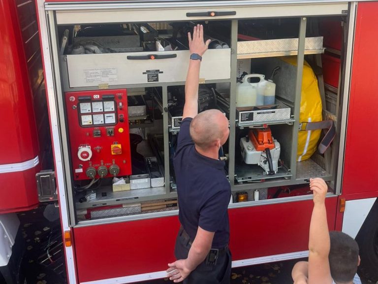 Feuerwehrmann zeigt auf Ausrüstung in einem roten Feuerwehrfahrzeug.