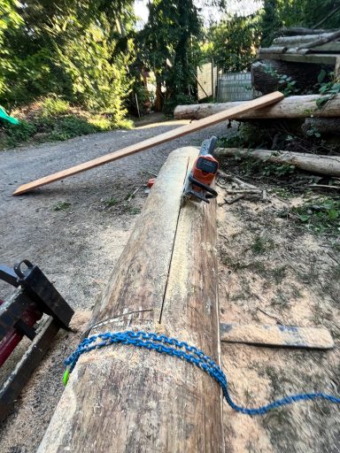 Rohes Holzstück auf dem Boden, mit Werkzeug und Holzstücken im Hintergrund.