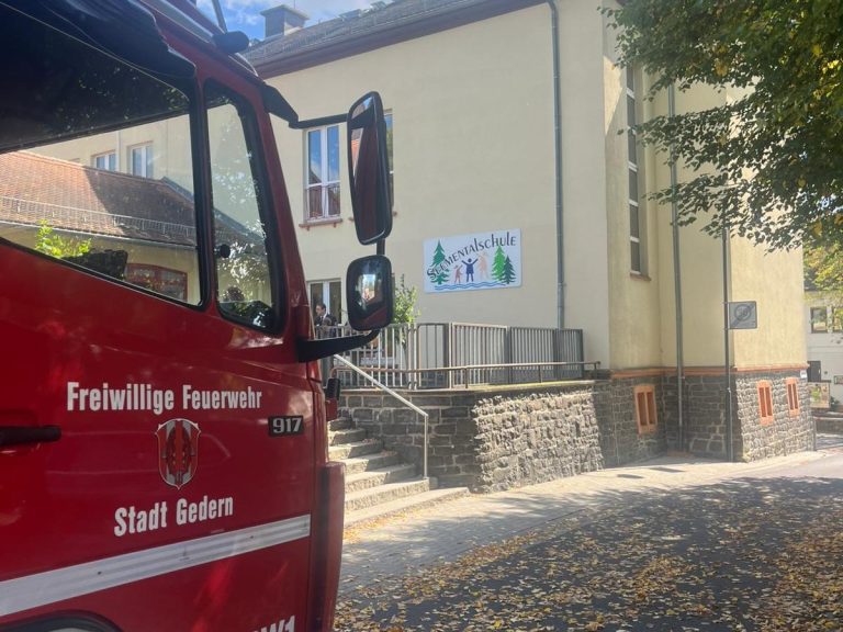 Rotes Feuerwehrfahrzeug vor einem Gebäude mit einer großen Werbetafel.