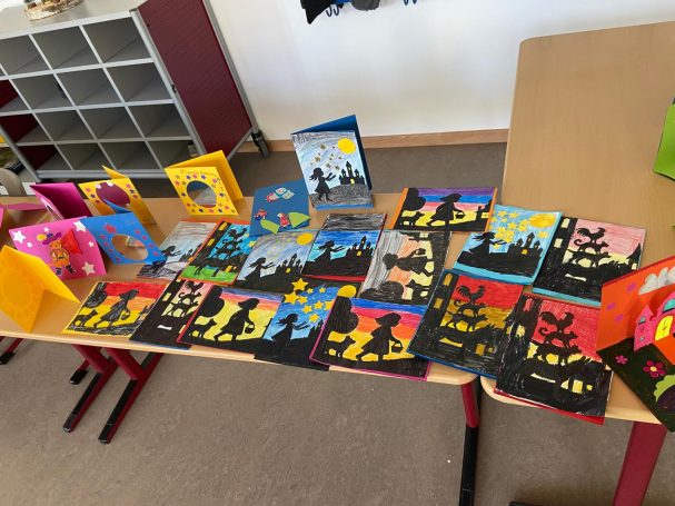 Bunte Kunstwerke auf einem Tisch, darunter Zeichnungen und Karten mit Stadtlandschaften.