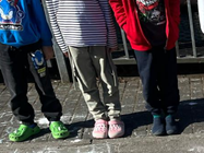 Fünf Kinderbeine in bunten Schuhen stehen nebeneinander auf einem Gehweg.