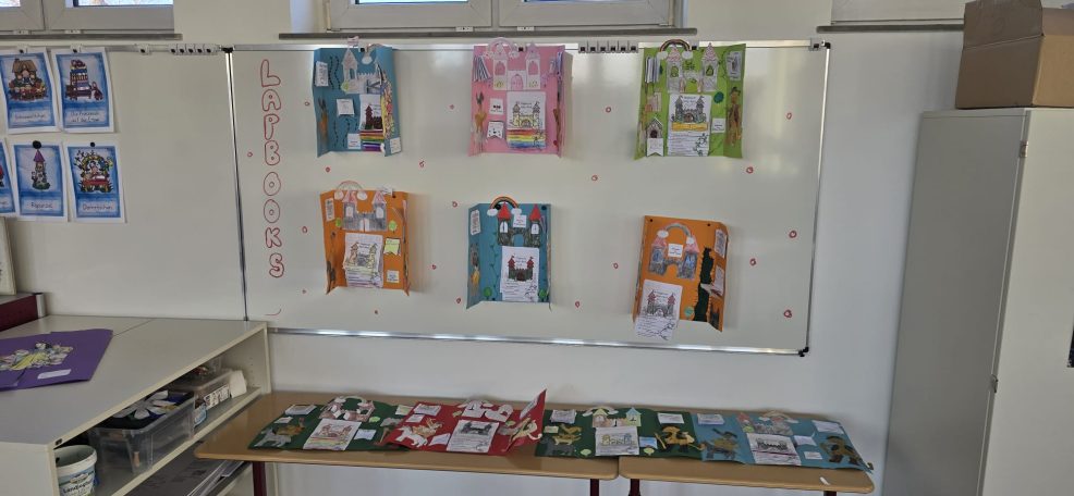 Ein Präsentationsbereich mit bunten Plakaten an einer Wand und Materialien auf einem Tisch.