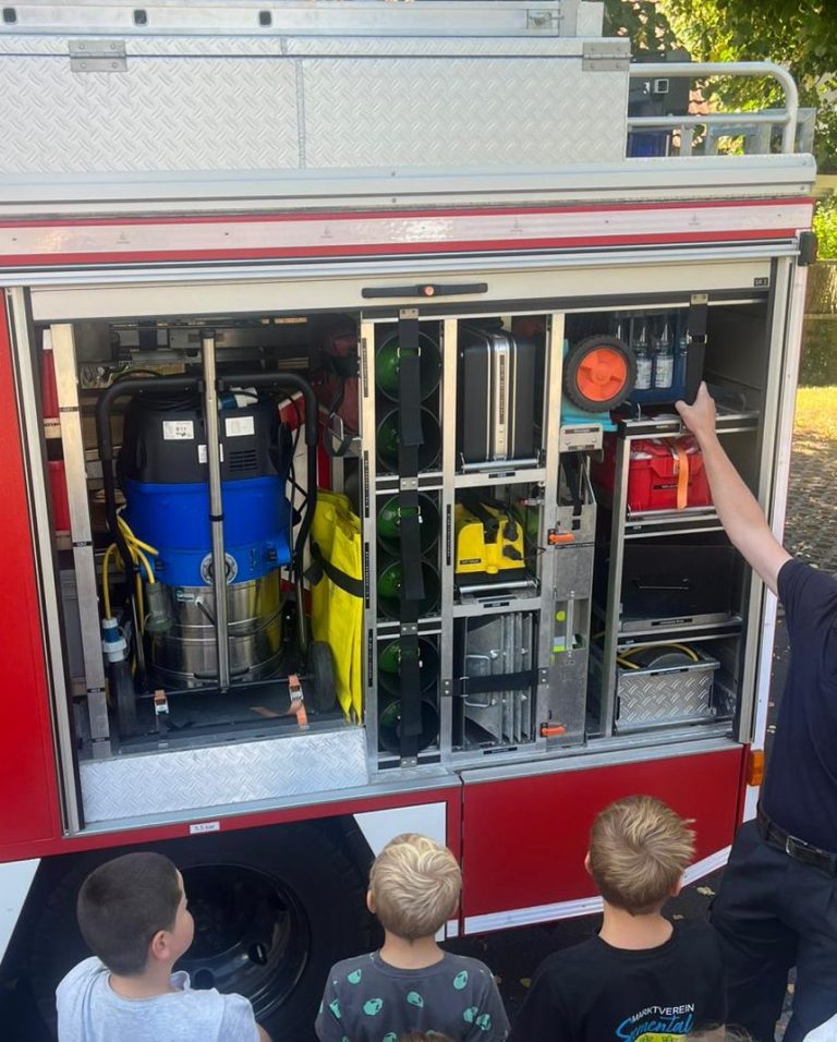 Feuerwehrmann erklärt Feuerwehrgeräte einer Gruppe neugieriger Kinder.
